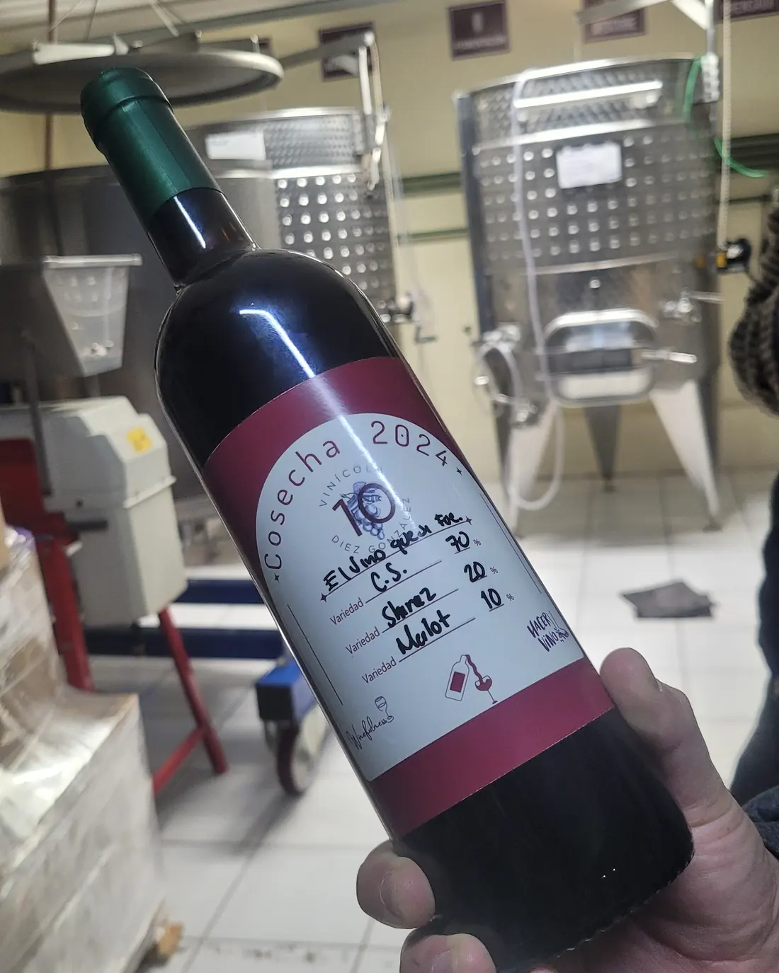 Botella de la cosecha 2024 de Vinícola Diez González frente a los tanques